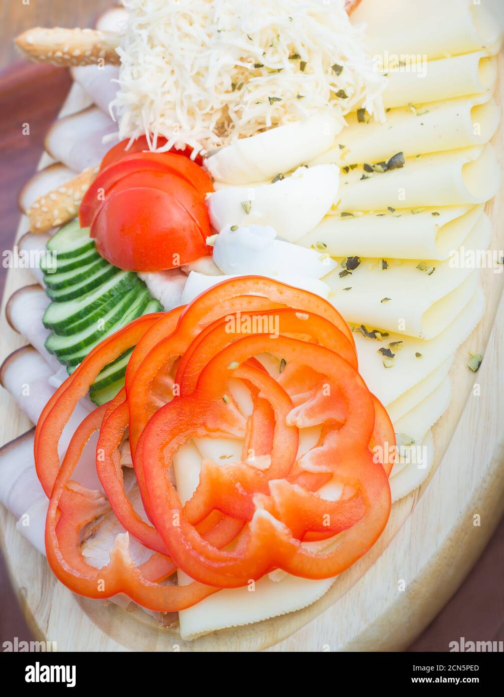 Simple slicing of assorted snacks: red pepper, cheese, ham on a wooden plate Stock Photo