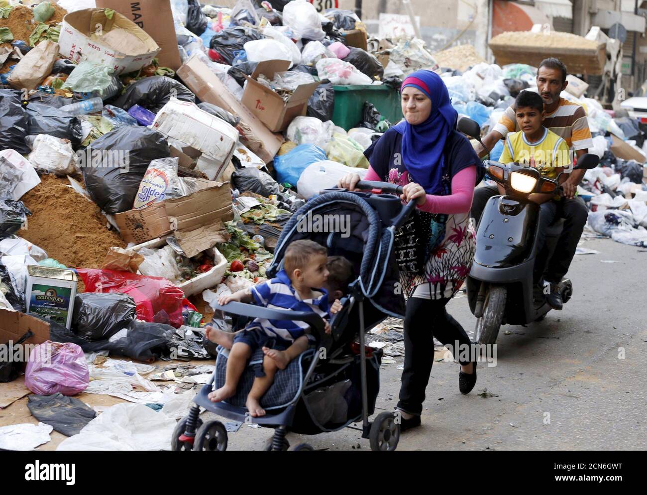 A woman pushes a stroller as other people ride on a scooter past garbage  piled up along a street in Beirut, Lebanon August 26, 2015. The powerful  Shi'ite party Hezbollah and its