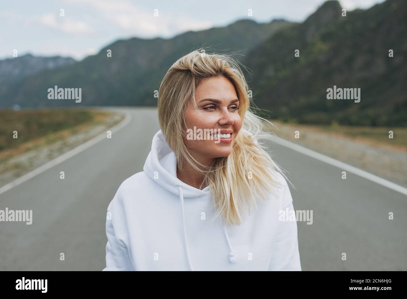 Beautiful smiling blonde young woman traveler in white hoodie on road trip to mountains Altai Stock Photo Alamy