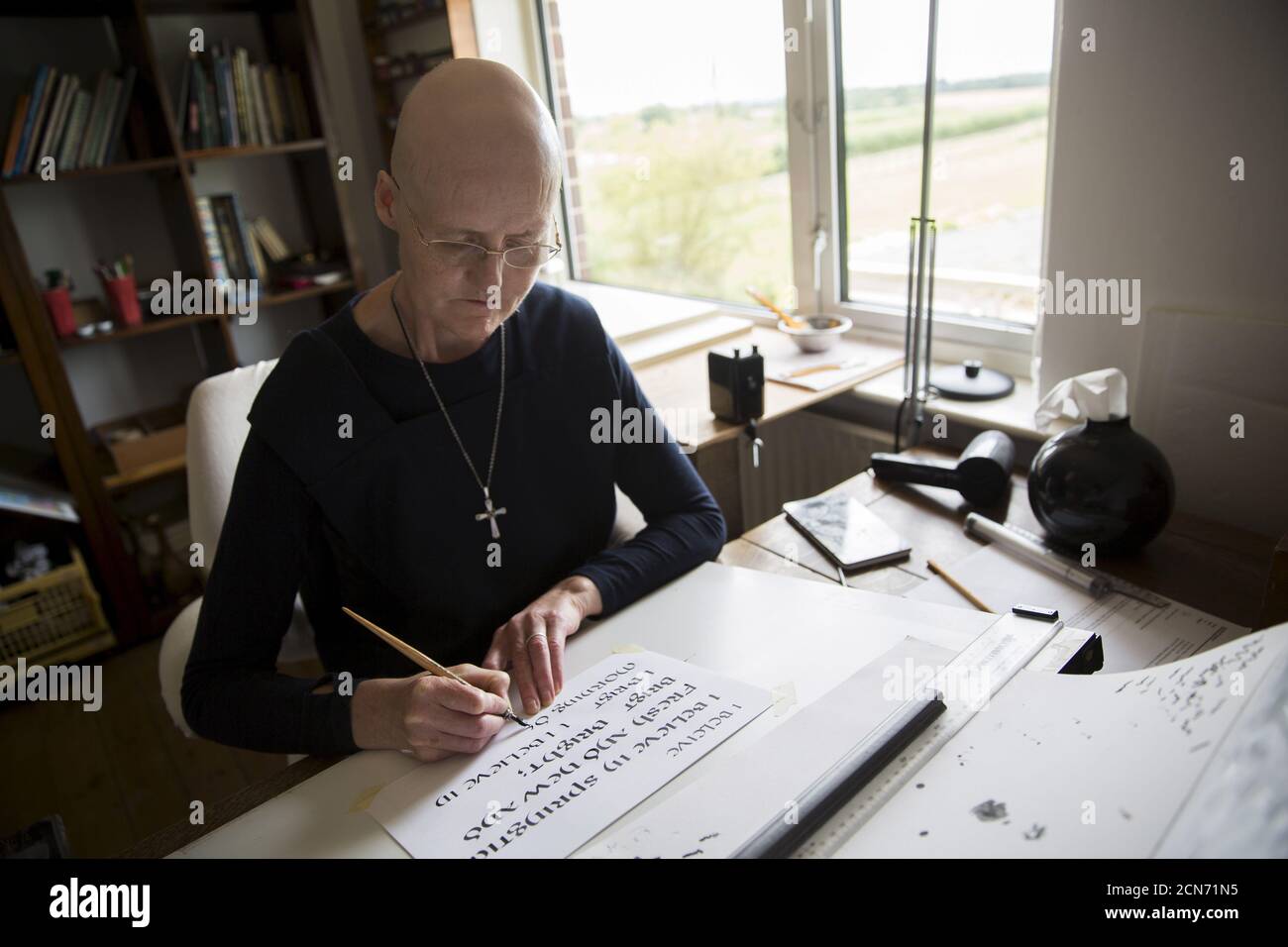 Sister Rachel Denton practices her calligraphy St Cuthbert's Hermitage in Lincolnshire, north east Britain August 24, 2015. Denton, a Catholic hermit, rises early to tend to her vegetable garden, feed her cats and pray. But the former Carmelite nun, who in 2006 pledged to live the rest of her life in solitude, has another chore - to update her Twitter account and check Facebook. 'The myth you often face as a hermit is that you should have a beard and live in a cave. None of which is me,' says the ex-teacher. For the modern-day hermit, she says social media is vital: 'tweets are rare, but preci Stock Photo