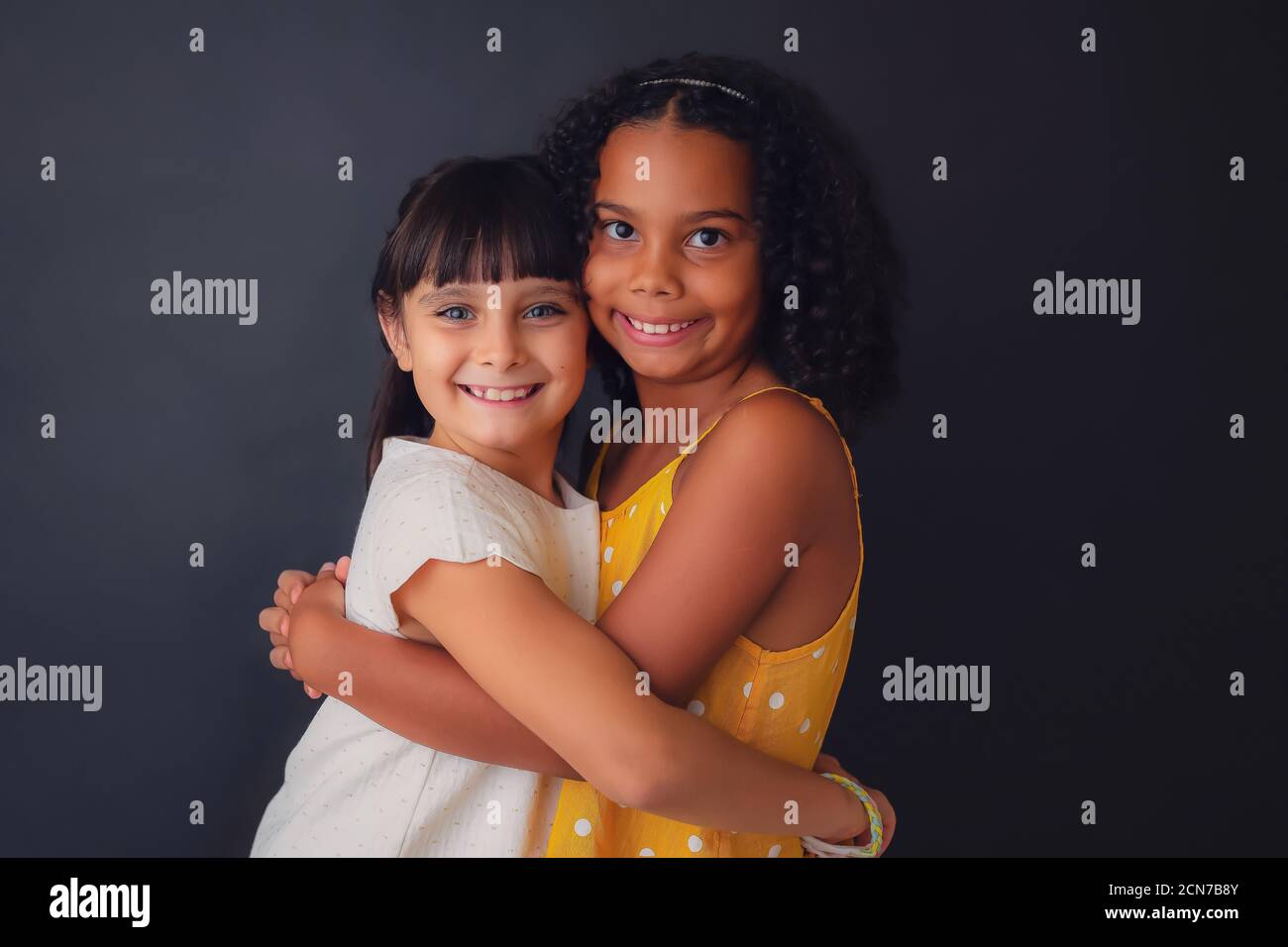 A 8-9 year old white girl and a 9-10 year old Africa American girl are hugging each other, and looking at the camera. They look happy and friendly. Stock Photo