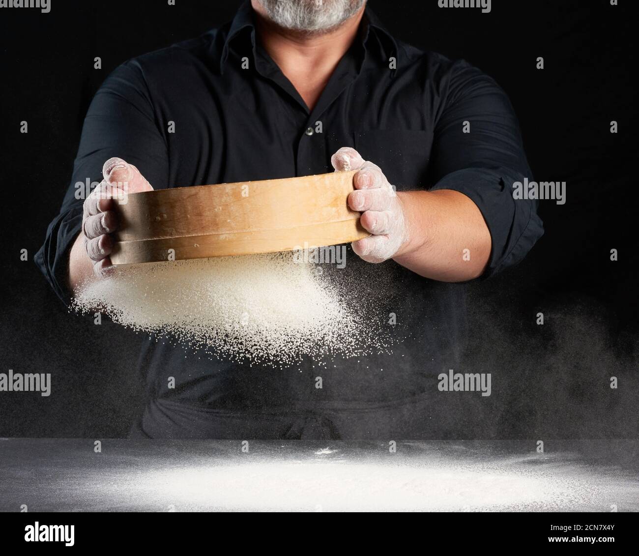 chef a man in a black uniform holds a round wooden sieve in his hands ...