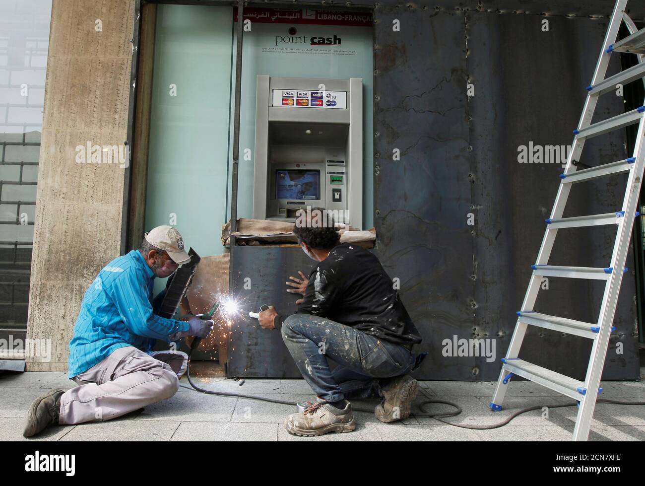 Workers board up an ATM machine at a branch of Banque Libano Francaise (BLF), as a protection measure amid protests against growing economic hardship, in Beirut, Lebanon April 30, 2020. REUTERS/Mohamed Azakir Stock Photo