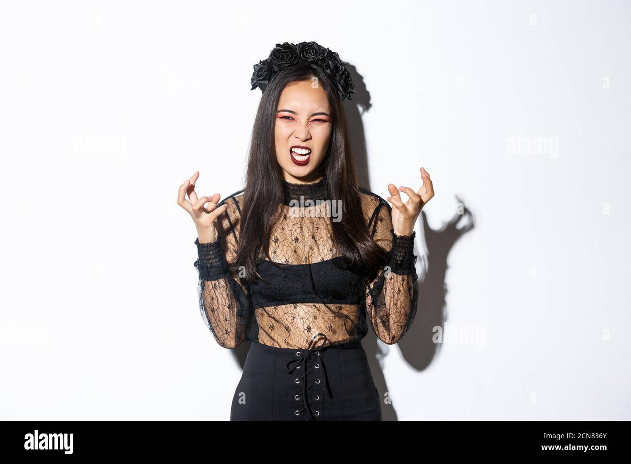 Image of woman in halloween costume looking like angry evil witch, cursing  and clenching fists mad. Female in black dress and wreath trick or treating  Stock Photo - Alamy