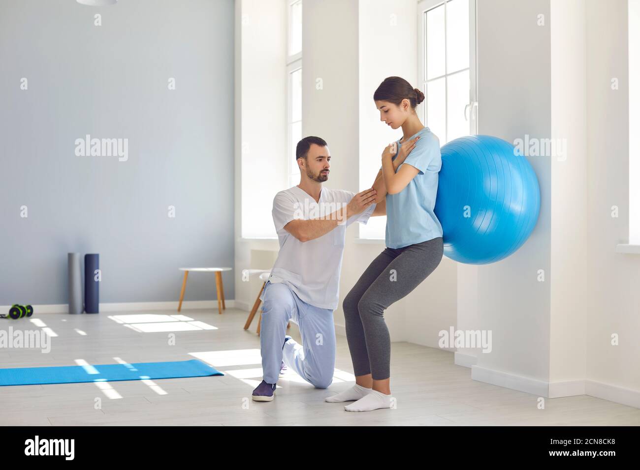 Physiotherapist helping young woman recover from back injury using big soft ball Stock Photo