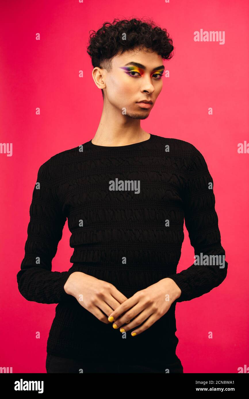 Portrait of a gay man in black t-shirt. Gender fluid man wearing black outfit posing against red background. Stock Photo