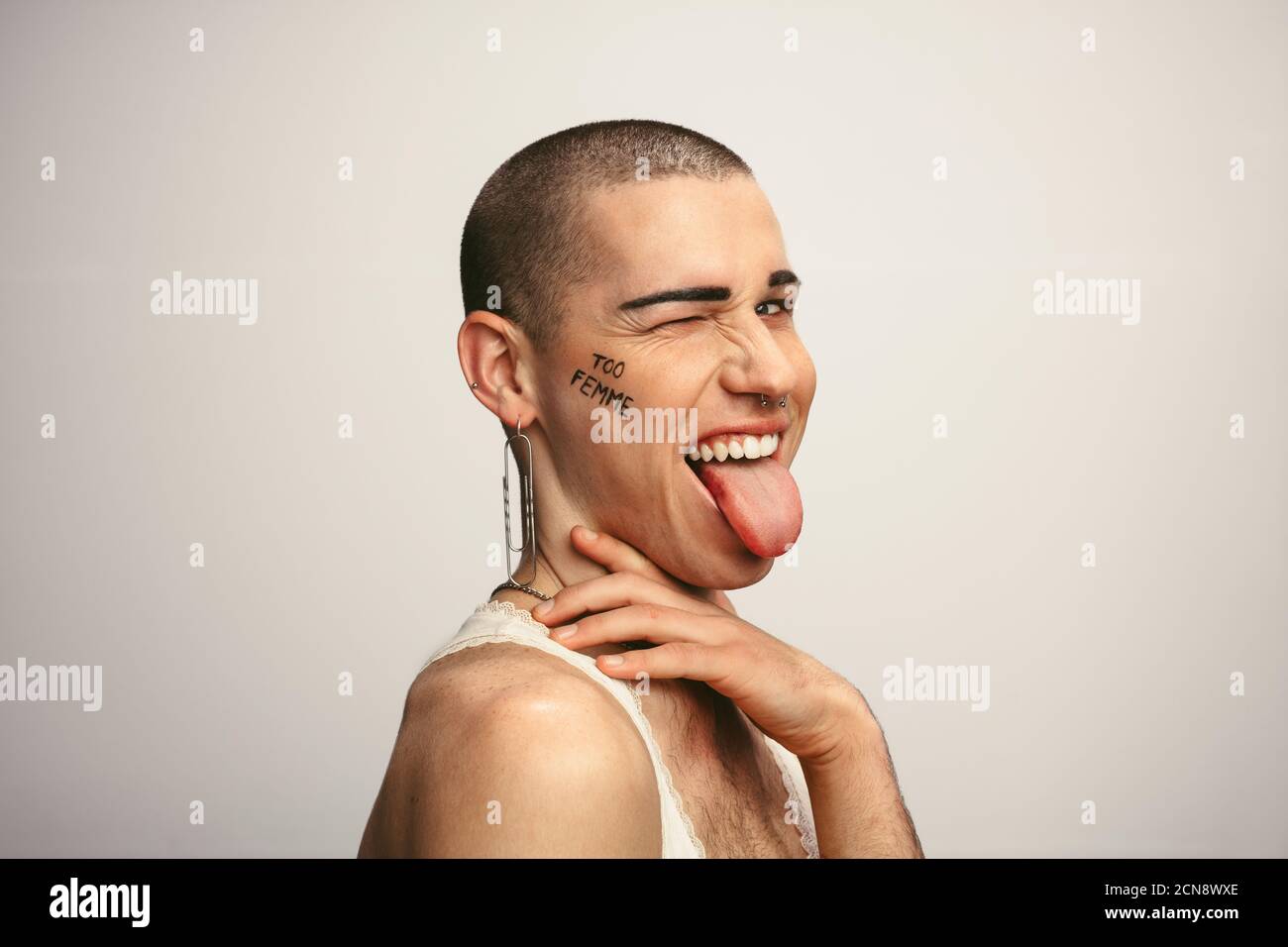 Gay man sticking out tongue and winking his eye. Gender fluid man making funny facial expressions on white background. Stock Photo