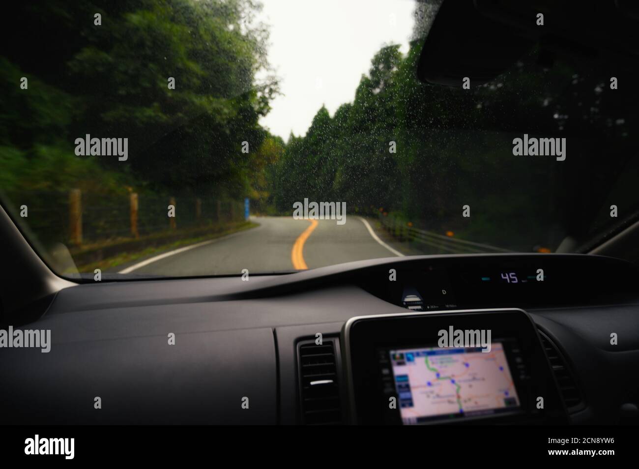 Road view in rainy season from a car windscreen that runs with care,   natural scenery surrounded with navigation device in the car at Japan. Stock Photo