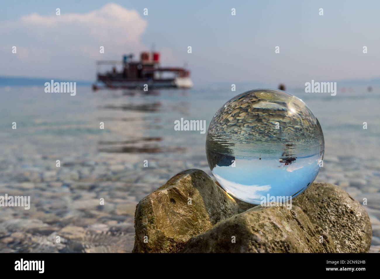 Crystal ball on stones near the sea. Original upside down view and rounded perspective of the sky, pebble seabed and boat. Original and engaging pictu Stock Photo