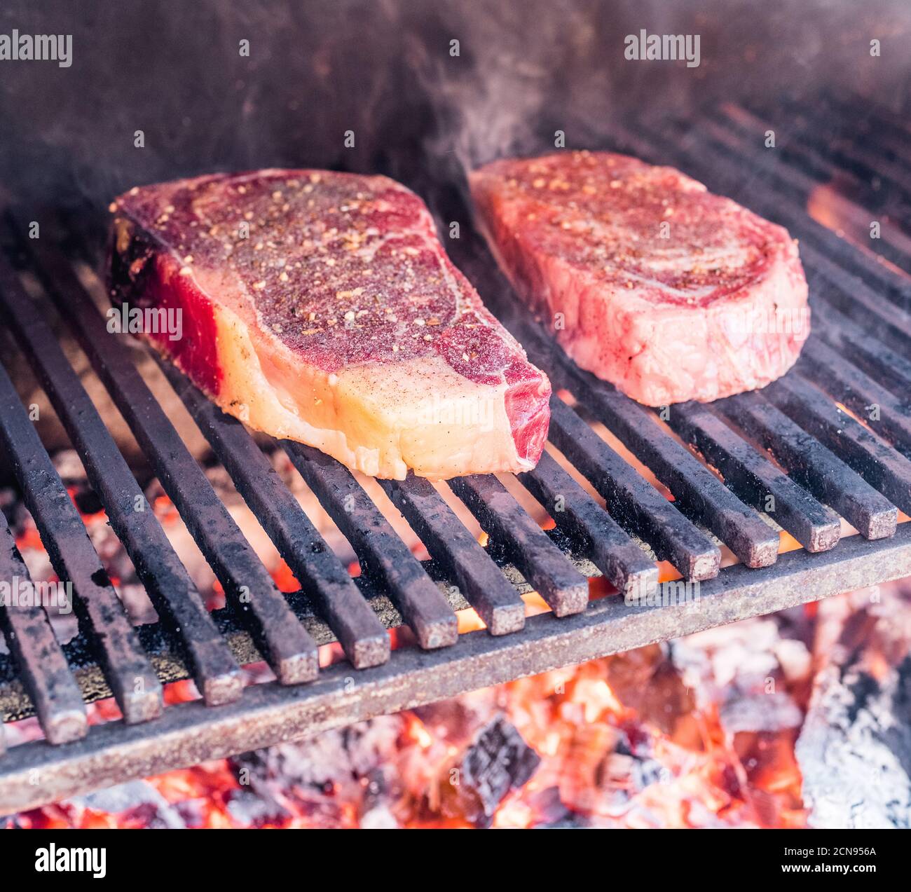 Steak ribeye cooking. Conceptual picture. Steak with spices and cutlery under burning grill grate. Stock Photo