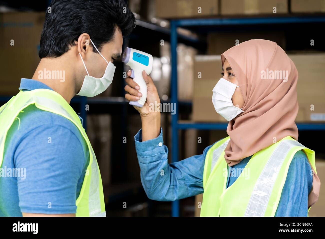 Islam Muslim asian warehouse worker take temperature to another worker Stock Photo