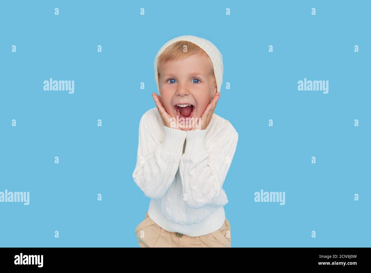 Wow face. Cute little blond boy in a warm white hat and sweater on a