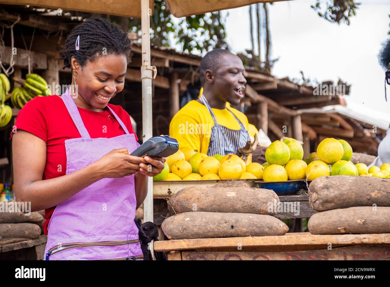 african woman selling in a local market using a pos machine and smiling