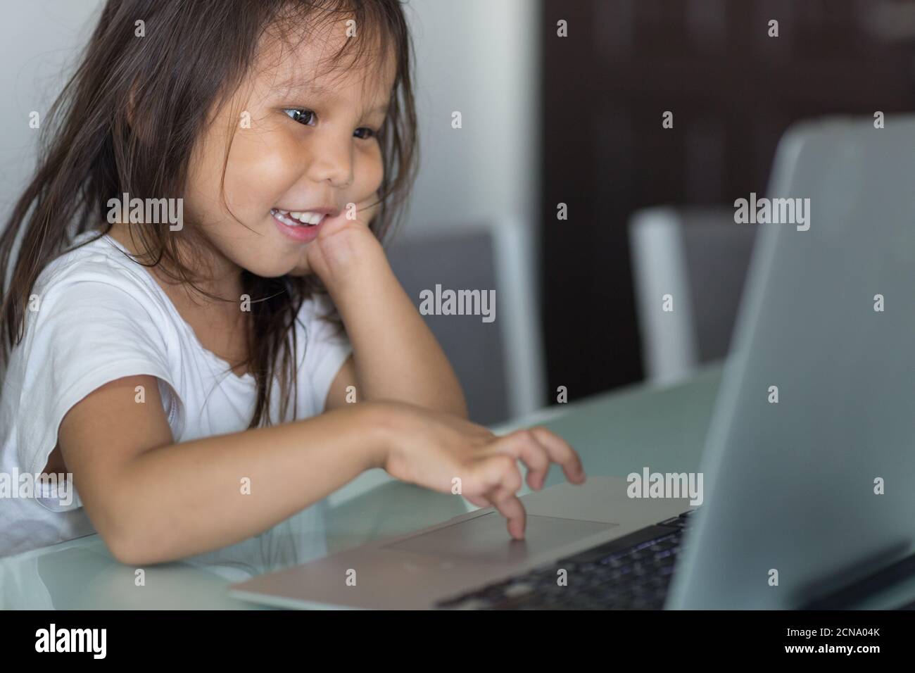 Cute little asian girl happy to use a laptop computer at home to homeschool. Stock Photo