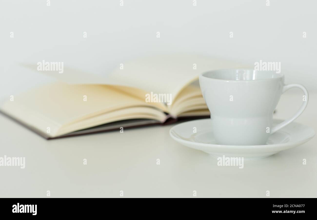 Open notebook with blank pages lying flat next to a coffee cup on a saucer. Isolated against white background. Calm study and relaxation. Stock Photo