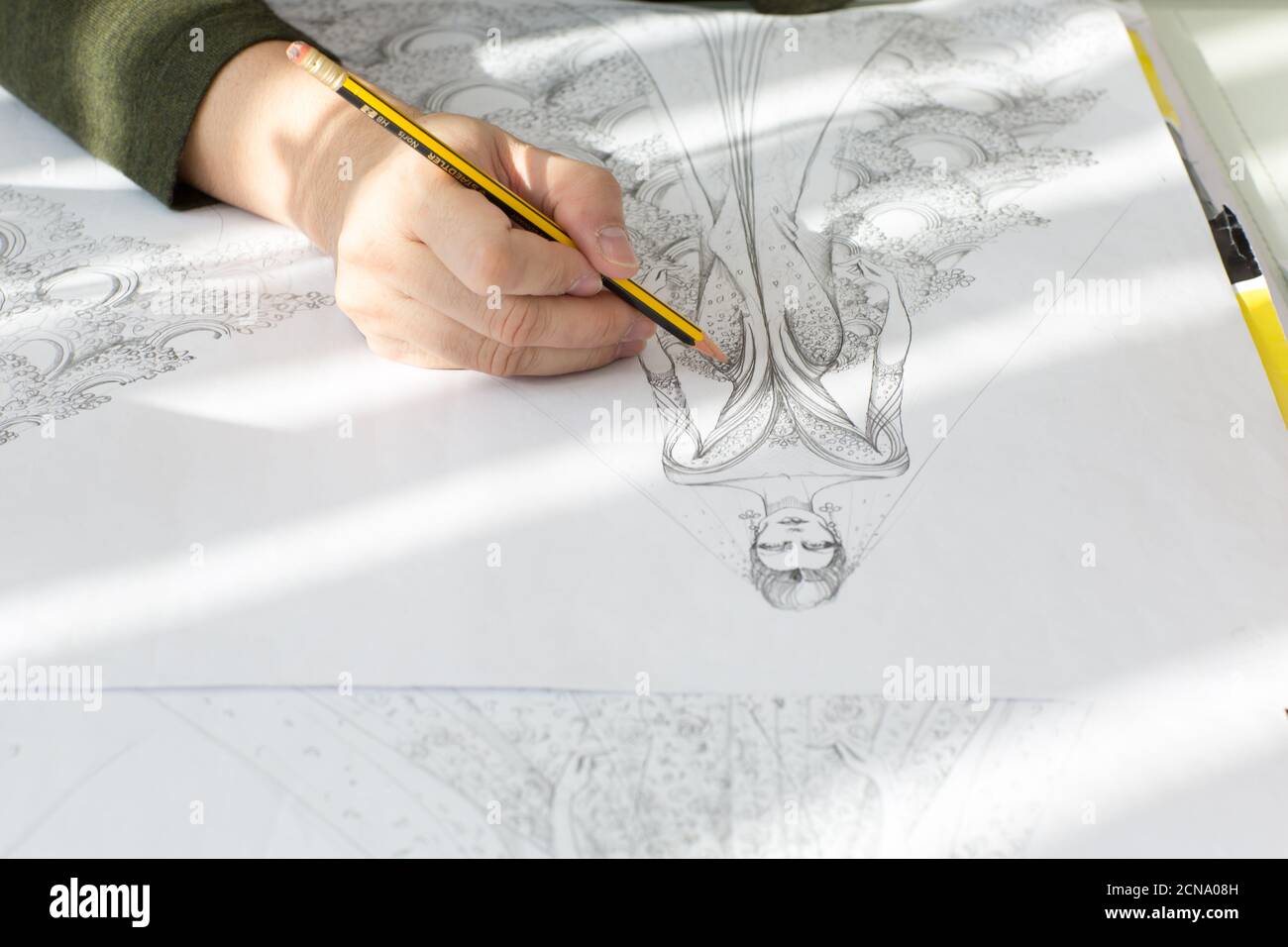 Fashion designer's hand sketching a haute couture wedding dress with a pencil on drawing paper. Stock Photo