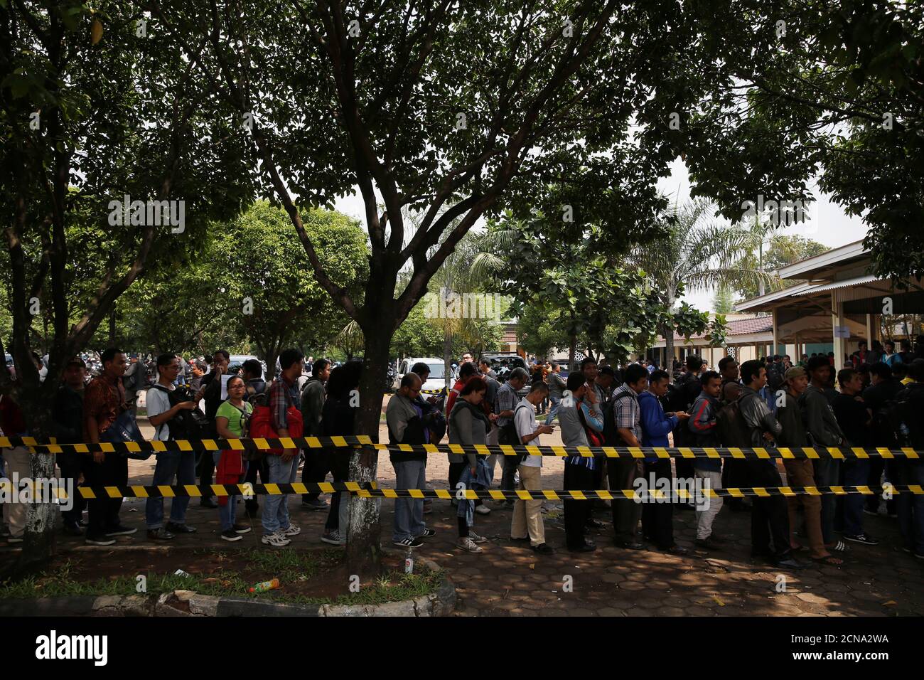 People queue under trees at an Uber motorcycle driver registration 