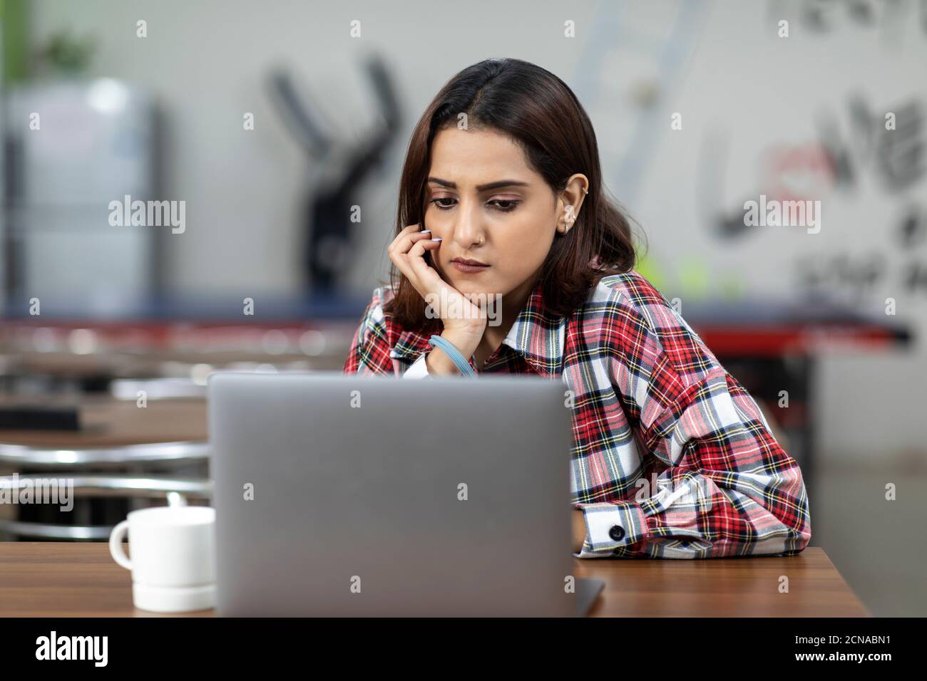Portrait of a tired Indian woman working on her laptop, sitting in an ...