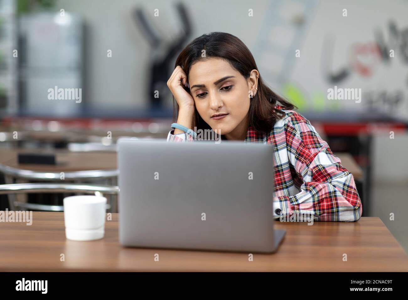 Portrait of a tired Indian woman working on her laptop, sitting in an ...