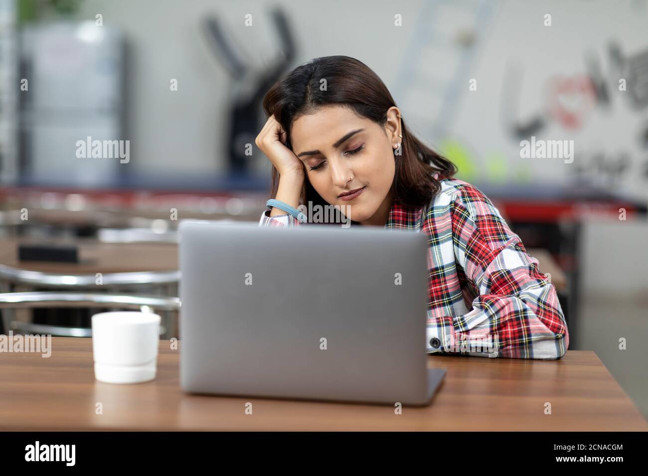 Portrait of a tired Indian woman working on her laptop, sitting in an ...