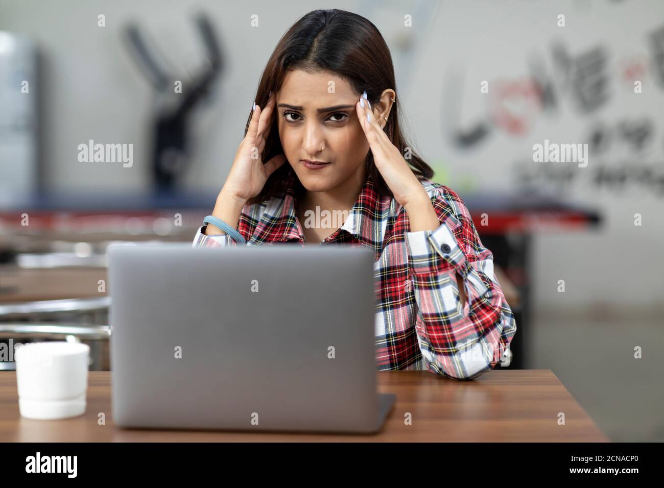 Portrait of a tired Indian woman working on her laptop, sitting in an ...
