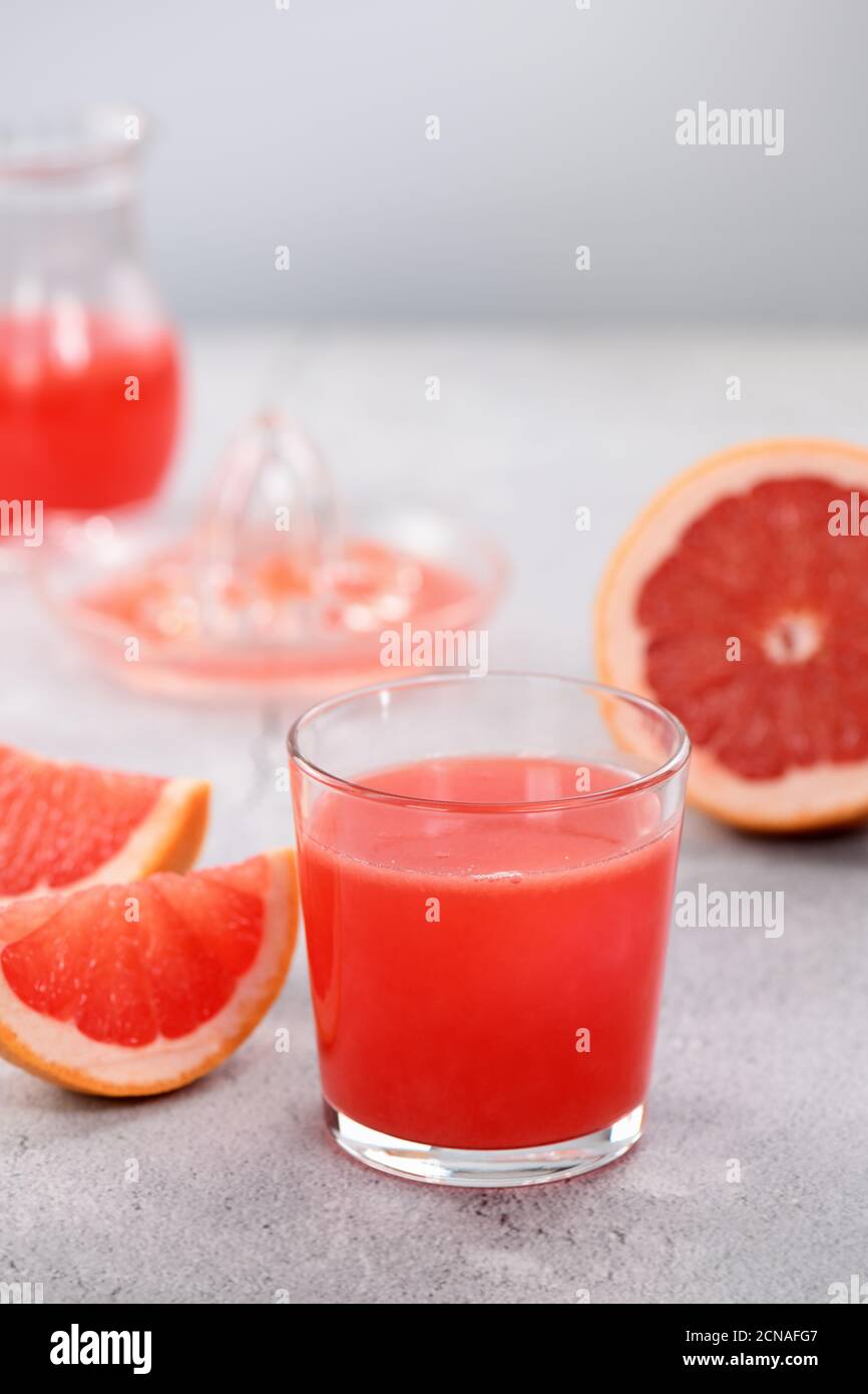 A glass of freshly made grapefruit juice and slices of fresh fruit on a light concrete background. H Stock Photo