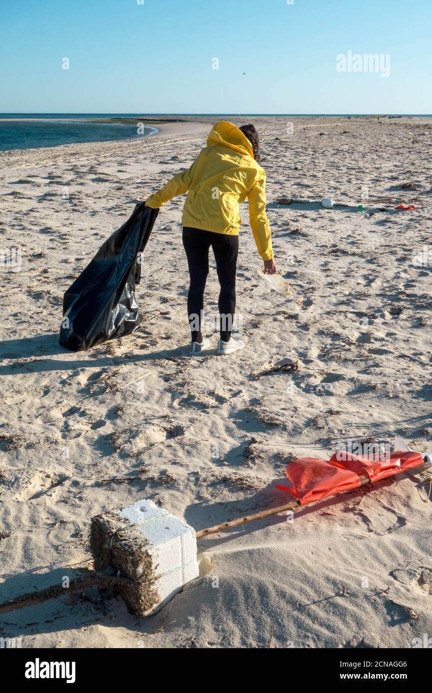 Woman picking up trash and plastics cleaning the beach with a garbage bag. Environmental volunteer activist against climate change and the pollution o Stock Photo
