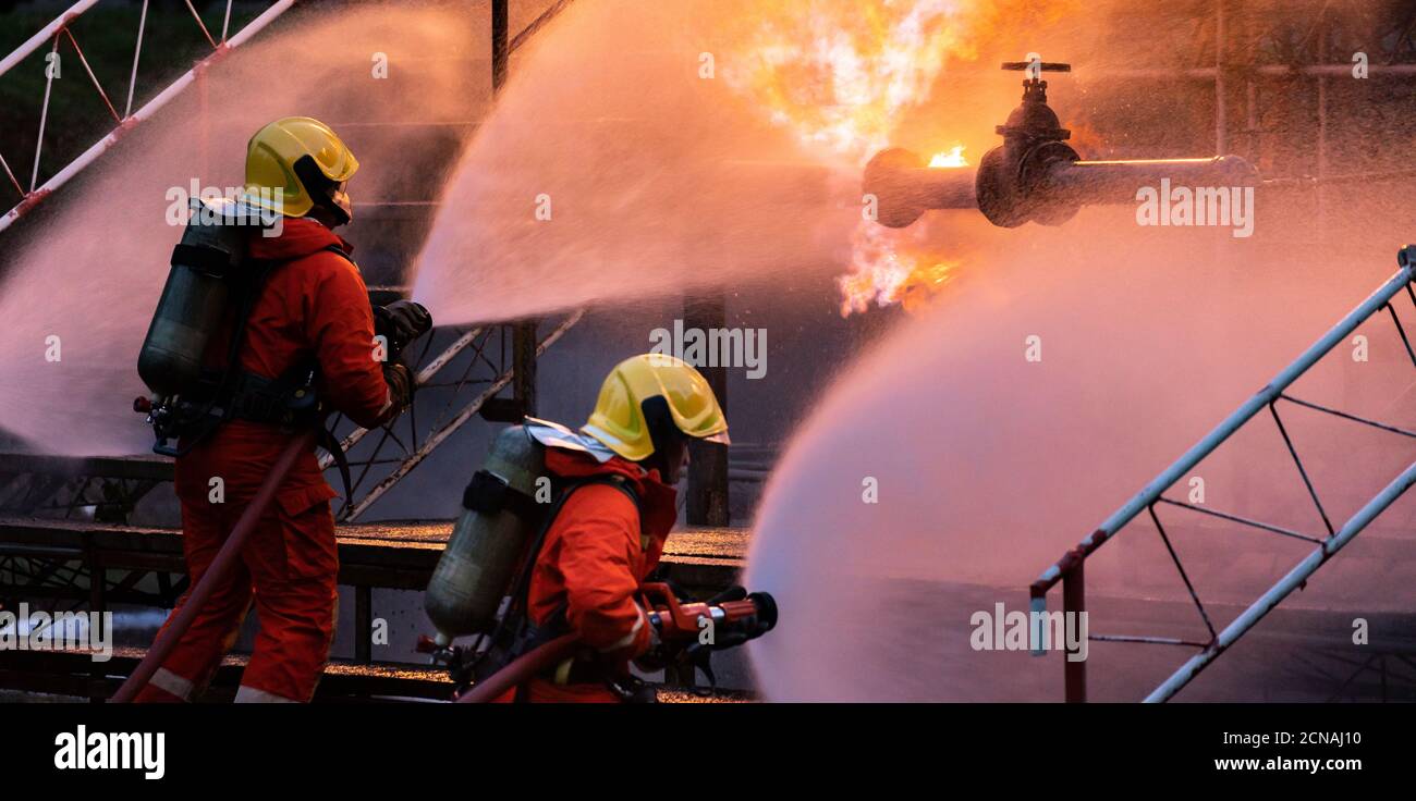 Panorama Firefighter team using water fog spraying down fire from oil rig factory explosion Stock Photo