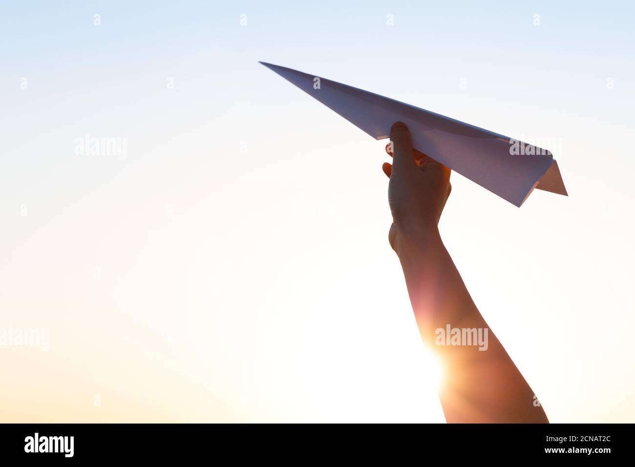The hand hold paper airplane and launch against the background of the bright sun Stock Photo