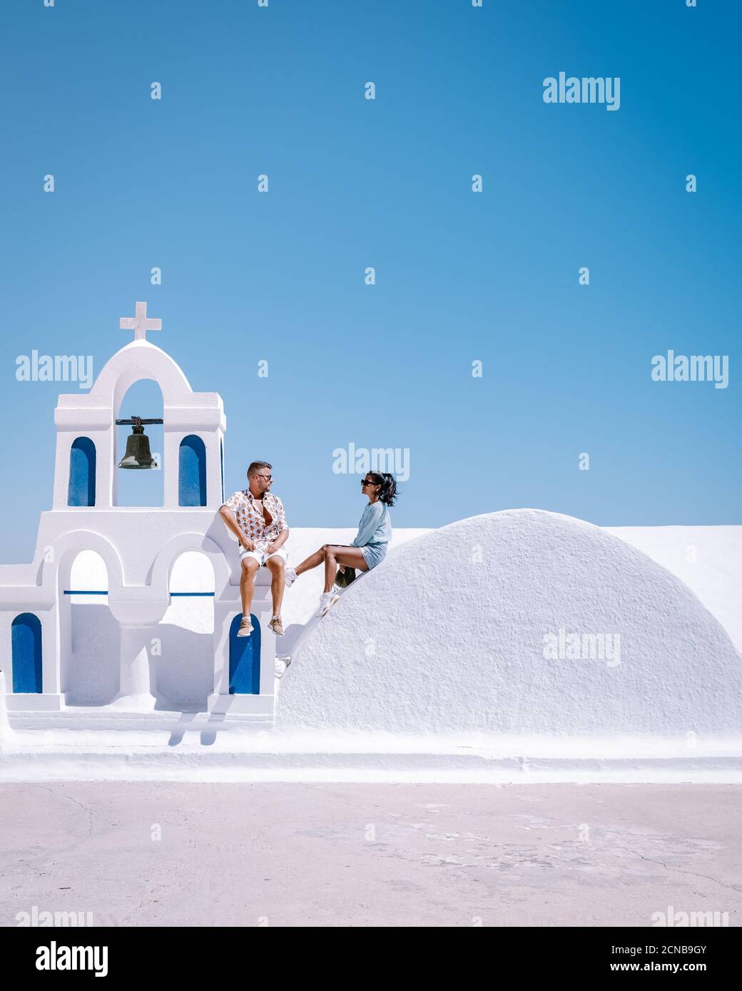 Santorini Greece, young couple on luxury vacation at the Island of Santorini watching sunrise by the blue dome church and whitew Stock Photo