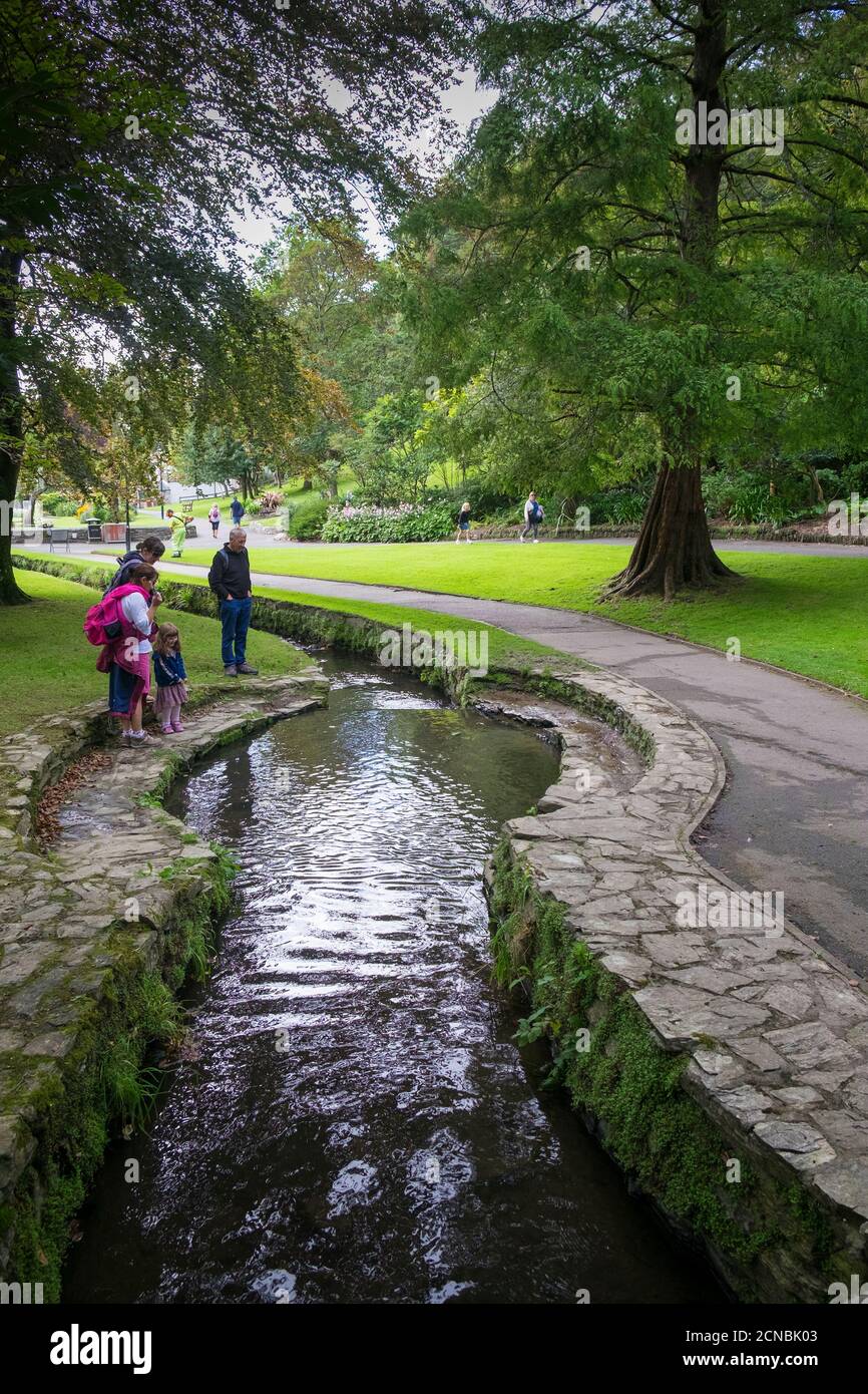 A family of holidaymakers watching leaves floating down the small river flowing through Trenance Gardens in Newquay in Cornwall. Stock Photo