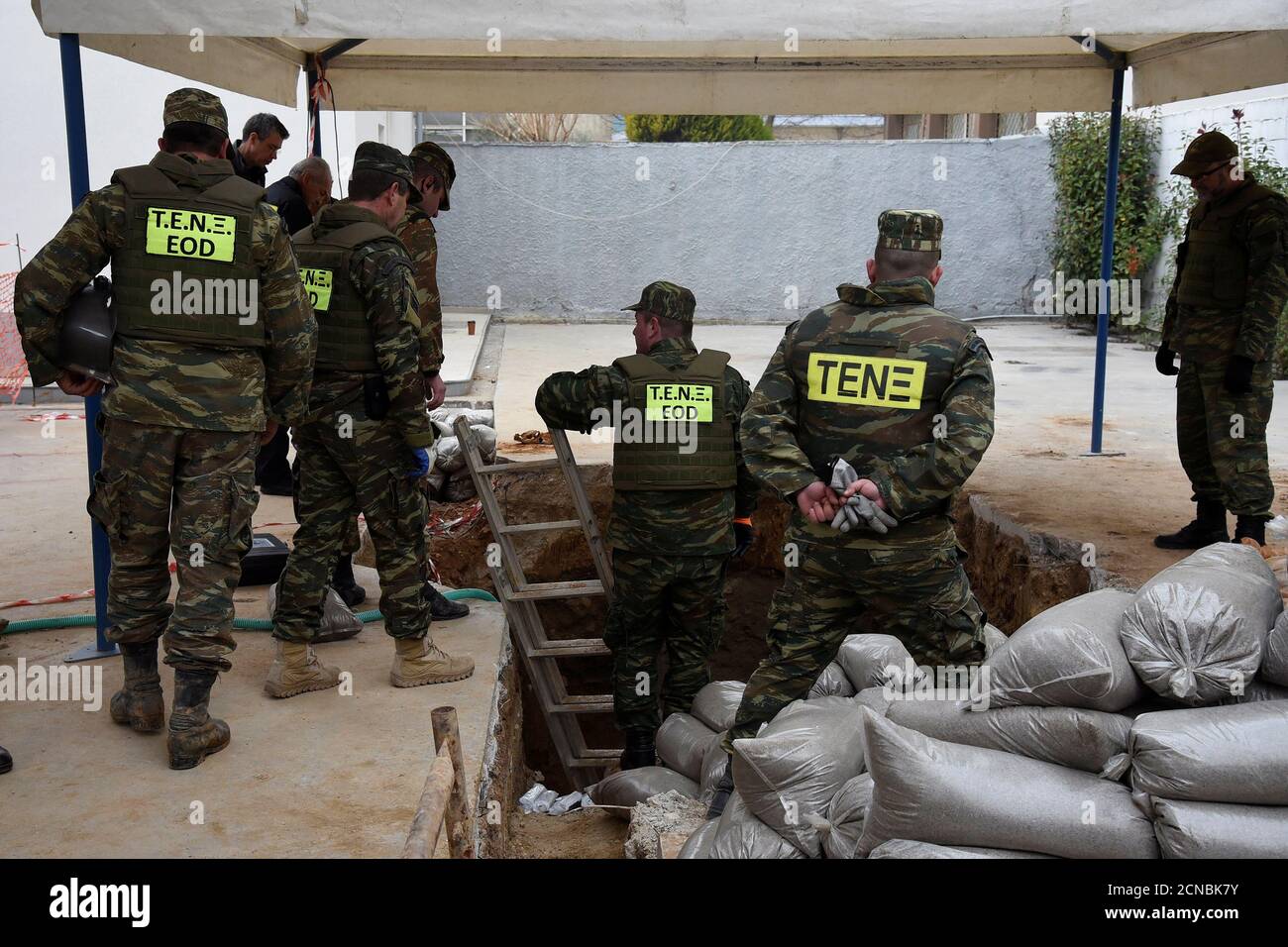 Military personnel of the Hellenic Army's Explosives Ordnance Disposal (EOD)  stand over a hole in the ground where a 250 kg World War Two bomb that was  found during excavation works at