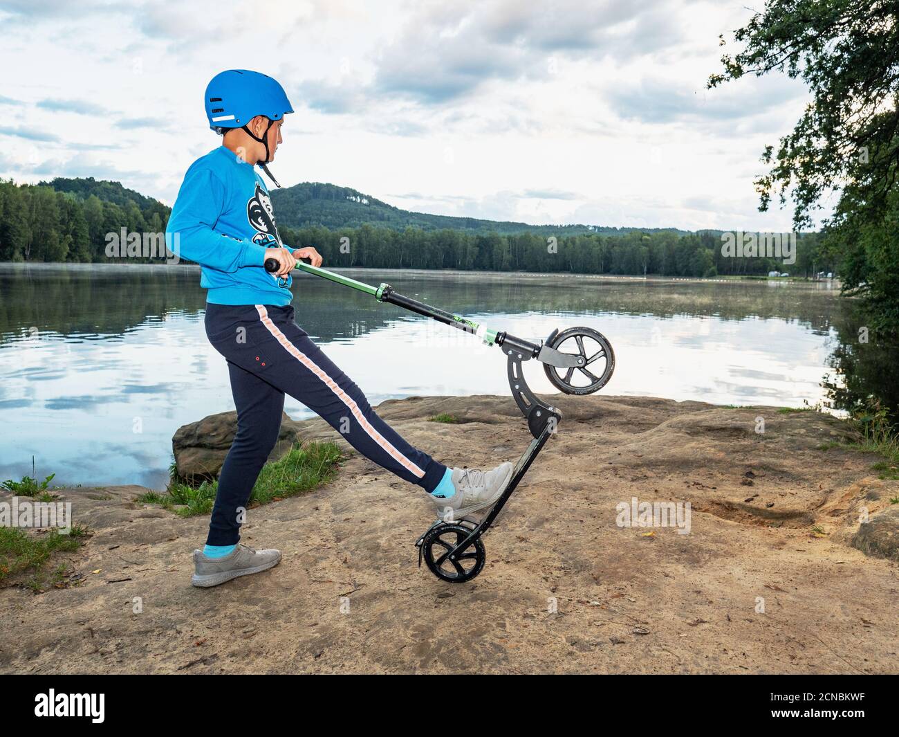 Boy with scooter makes trick on rocky lake bank Stock Photo