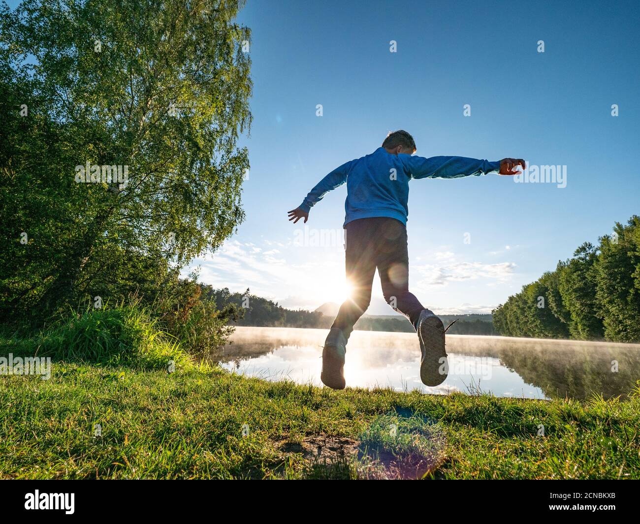Crazy boy is making fun and jumping on lake bank Stock Photo