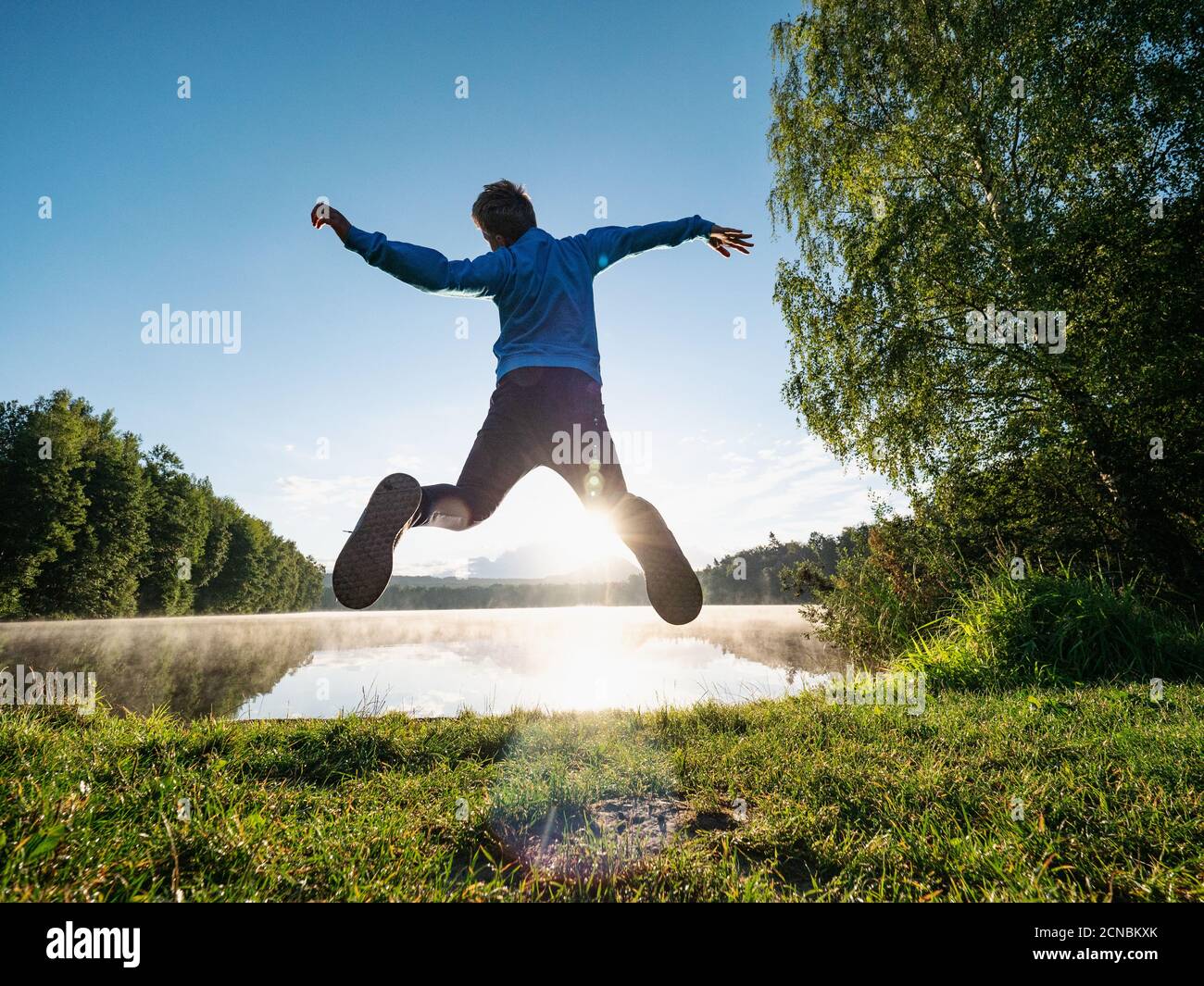 Jumping short hair boy at mountain lake makes fun Stock Photo