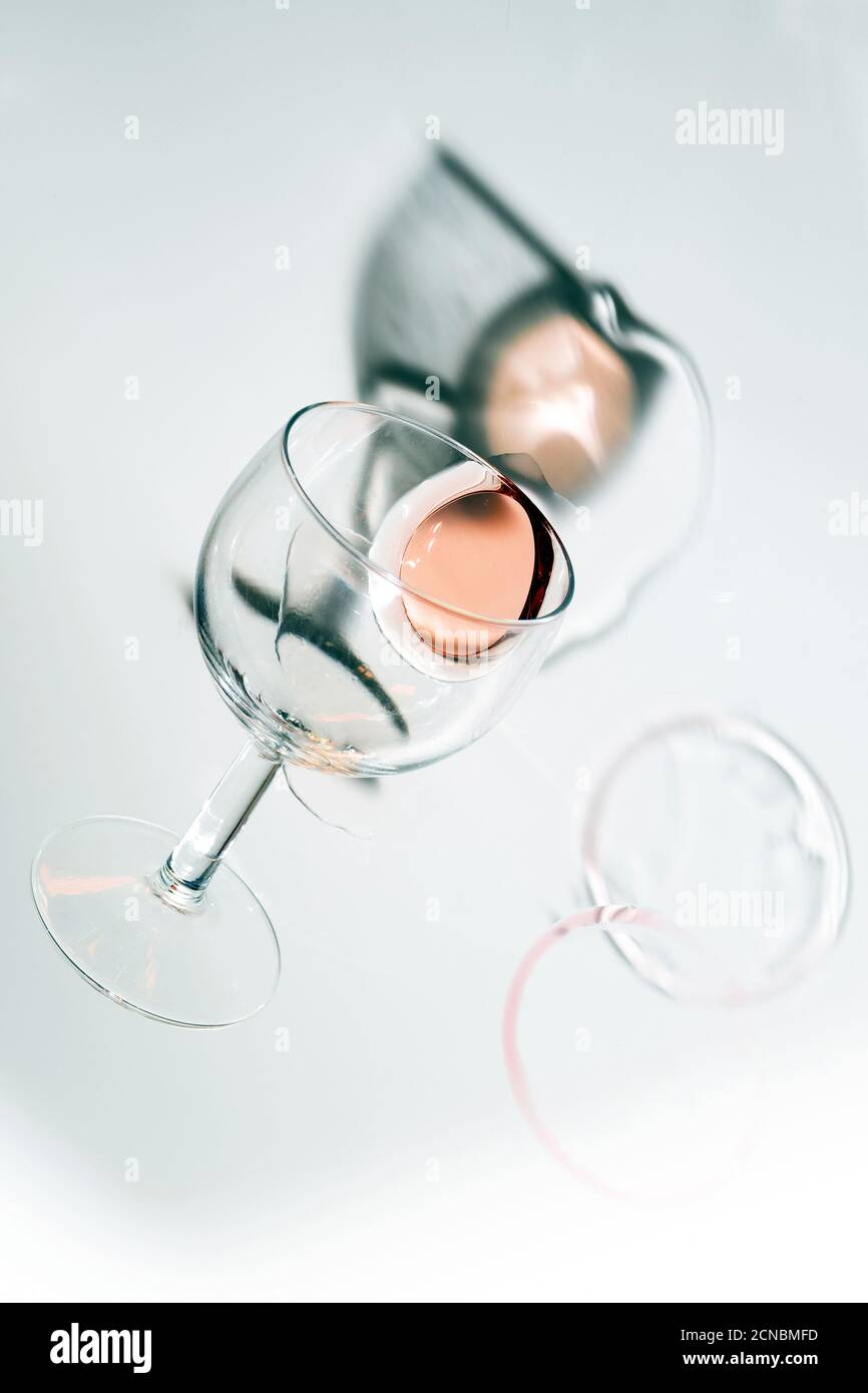 Overturned glass with a puddle of rosé wine, unusual perspective, reflection and shadows, abstract party concept or alcohol addiction, bright gray bac Stock Photo