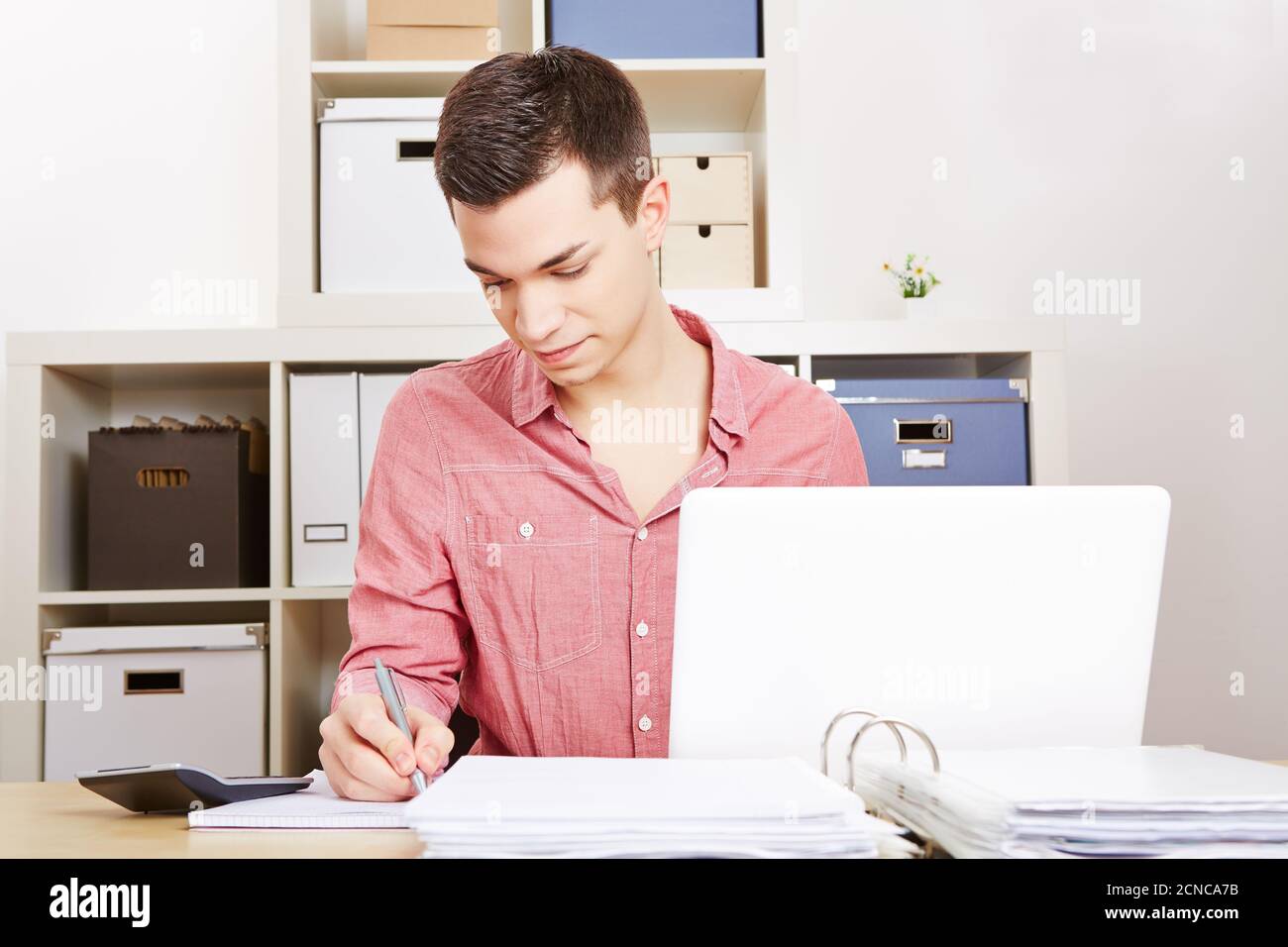 Young man works on computer in office and takes notes Stock Photo