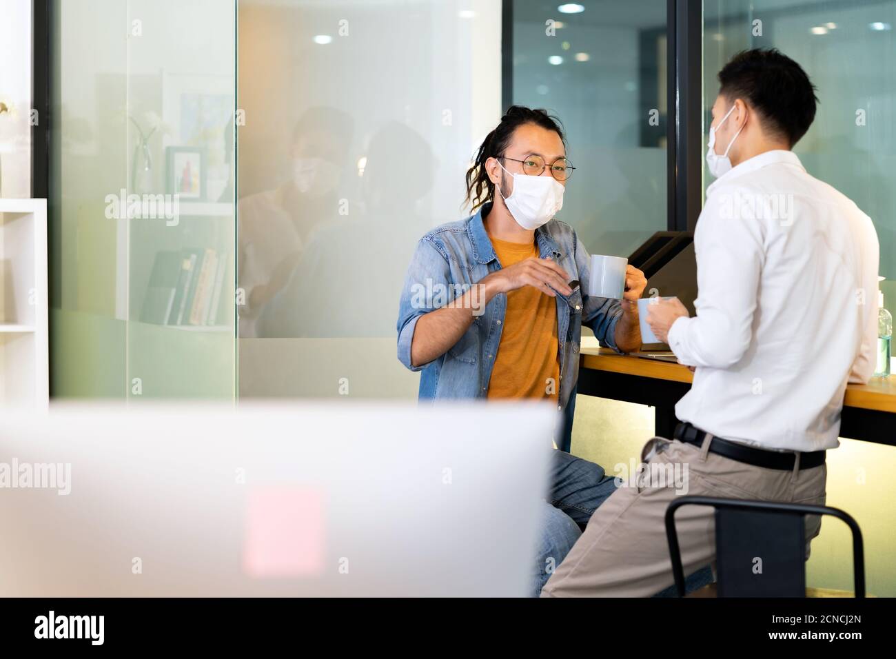 Two office workers talking while coffee break in new normal office. Stock Photo