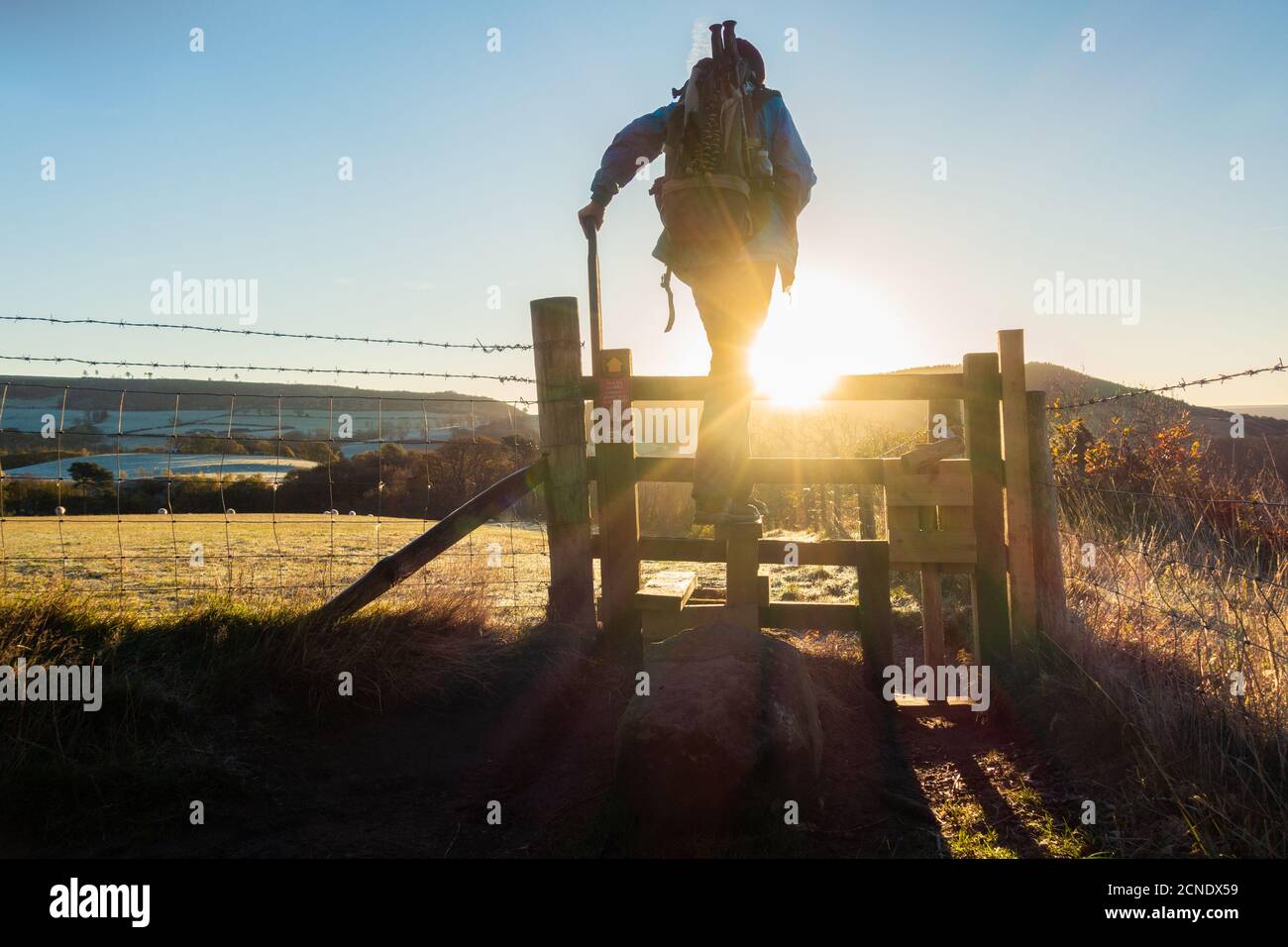 Rear view of hiker crossing stile at sunrise on a frosty November morning. North York Moors National Park, North Yorkshire, England. UK Stock Photo