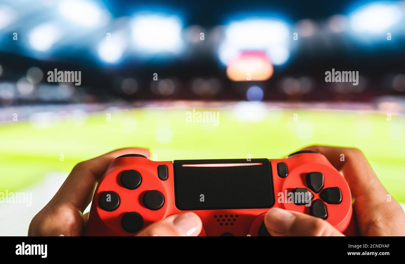 Young man having fun playing online soccer video games - Close up red magma game pad on tv background Stock Photo