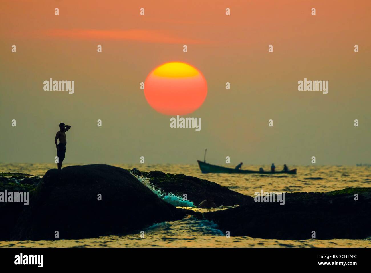 Man on intertidal rocks and fishing boat at sunset on beautiful unspoilt Kizhunna Beach, south of Kannur, Kannur, Kerala, India, Asia Stock Photo