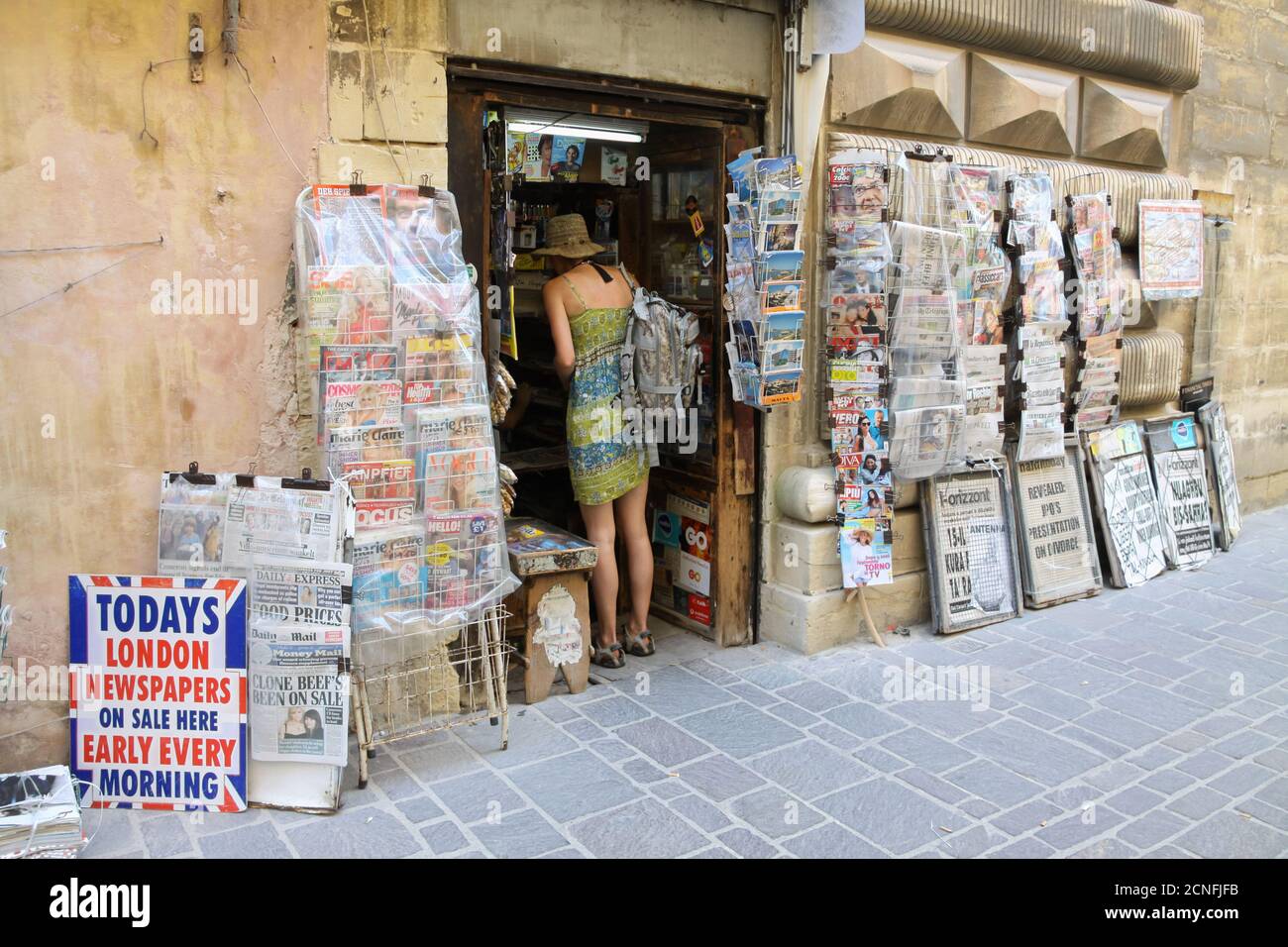 A woman buying a newspaper at a newsagent selling British papers in Valletta, Malta Stock Photo