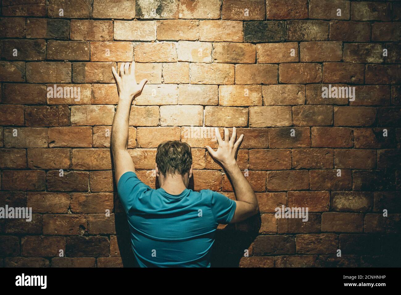 Rear view man under life crisis problems stand facing brown brick wall