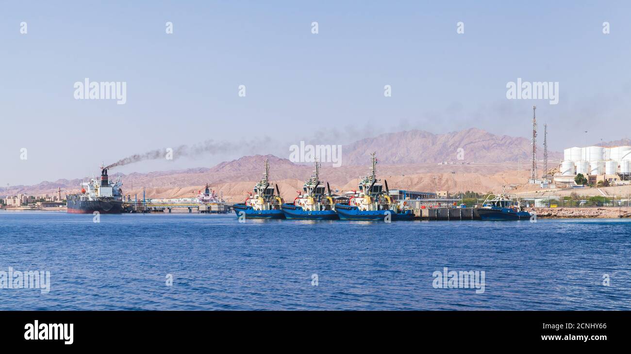 Tug boats and cargo ships are moored in Aqaba Port at sunny day, Jordan Stock Photo