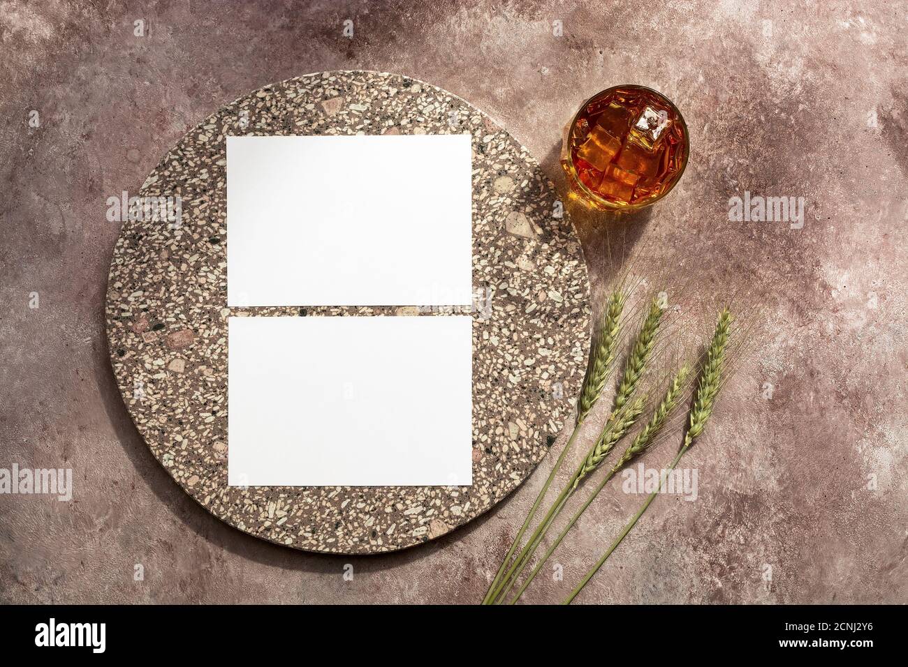 Whiskey glass with ice, blank white business card mockup with elements of granite and ears of wheat. Male background. Alcohol industry template. Top v Stock Photo