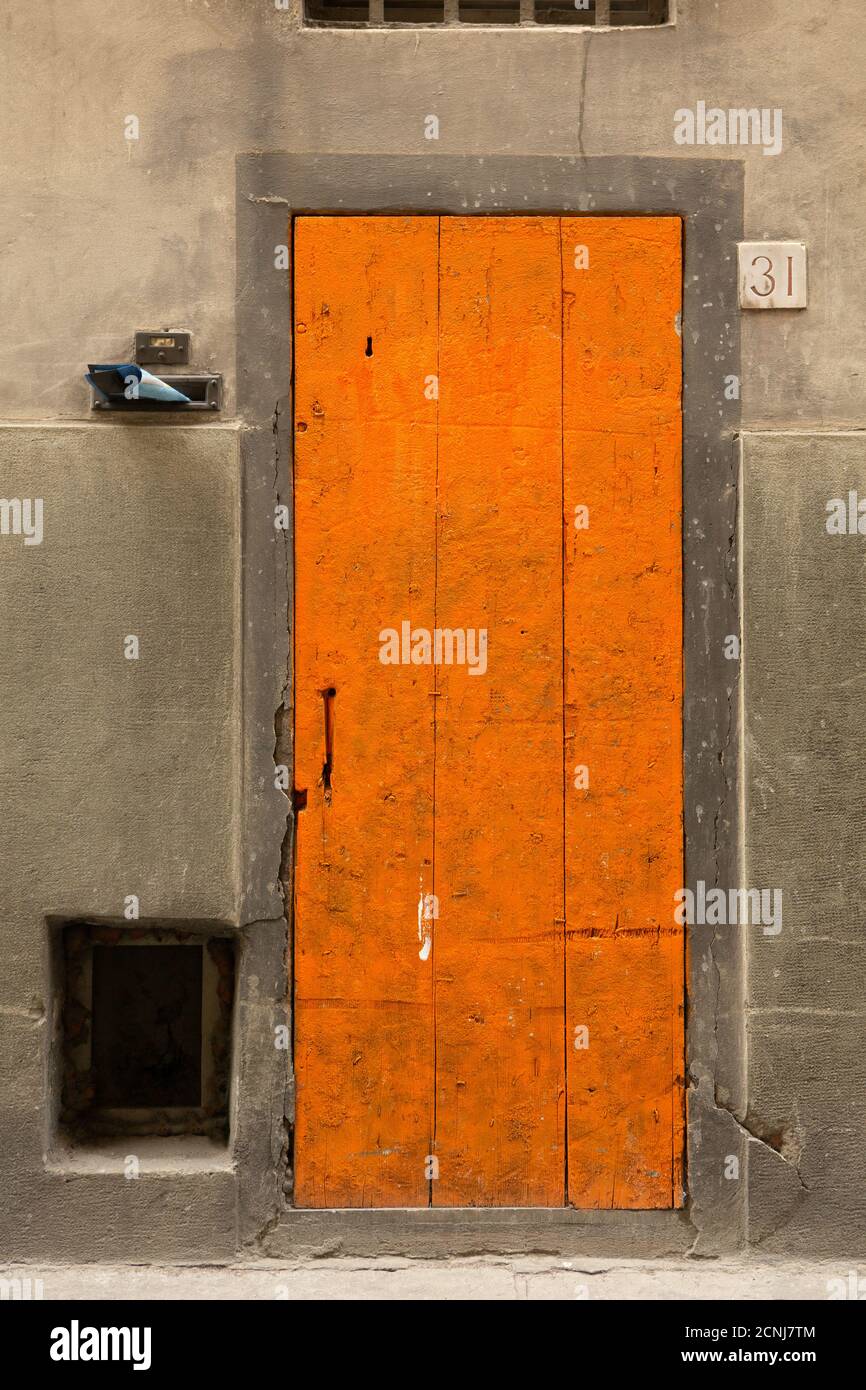 Wooden front door and house number 31 on old wall. Orange door on gray background. May, 2013. Pisa, Italy Stock Photo