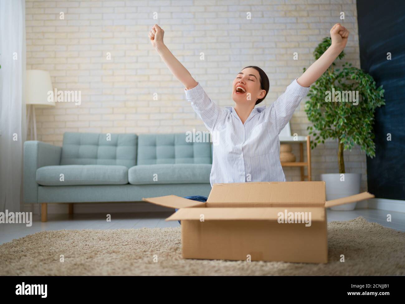 Beautiful young woman is holding cardboard box sitting on sofa at home ...
