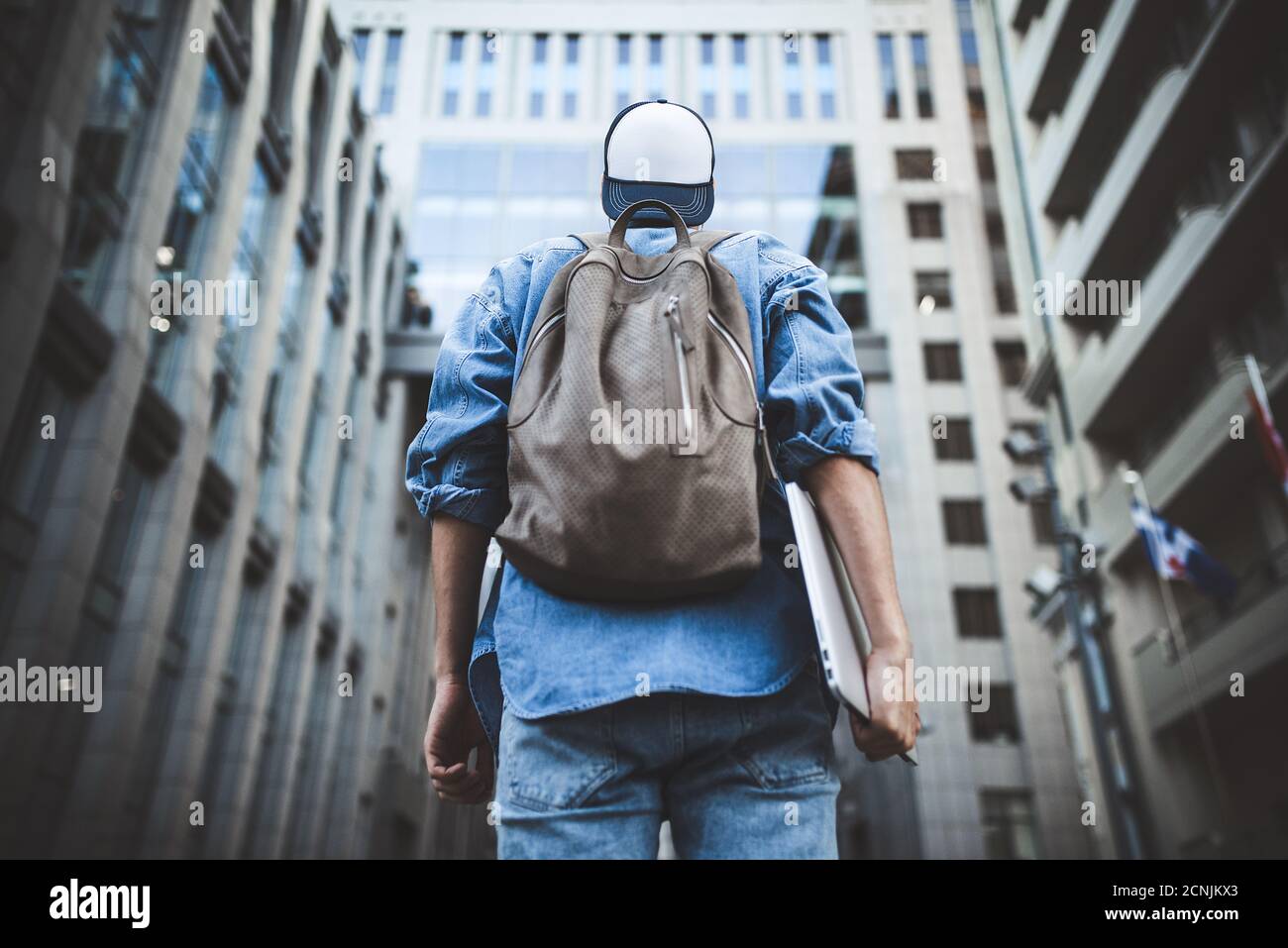 Cheerful young man with backpack enjoying walk the city with laptop and snap back. Stock Photo