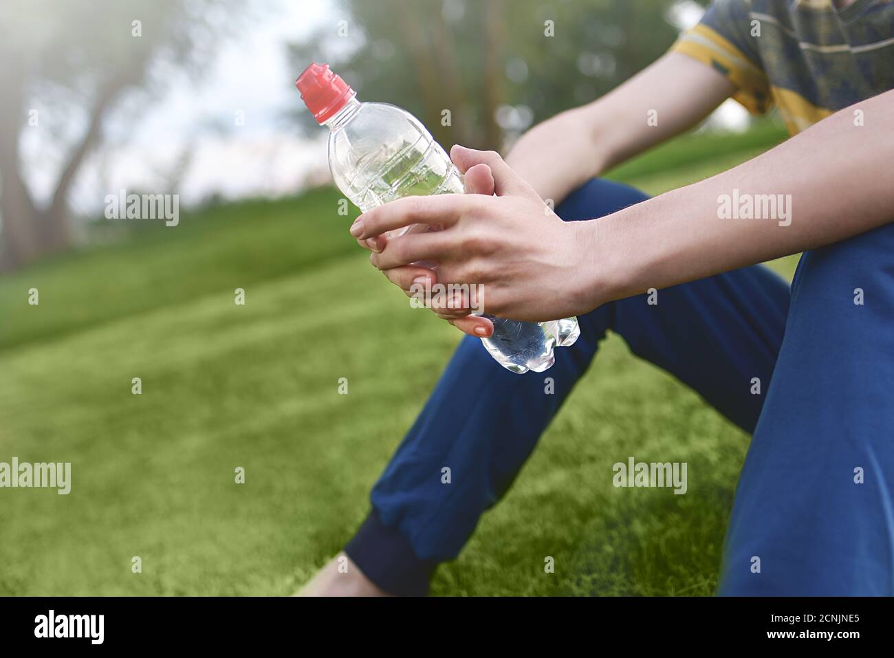 https://c8.alamy.com/comp/2CNJNE5/young-caucasian-man-runner-relaxing-holding-drinking-water-bottle-and-sitting-on-grass-in-the-park-outdoors-after-sport-at-early-2CNJNE5.jpg