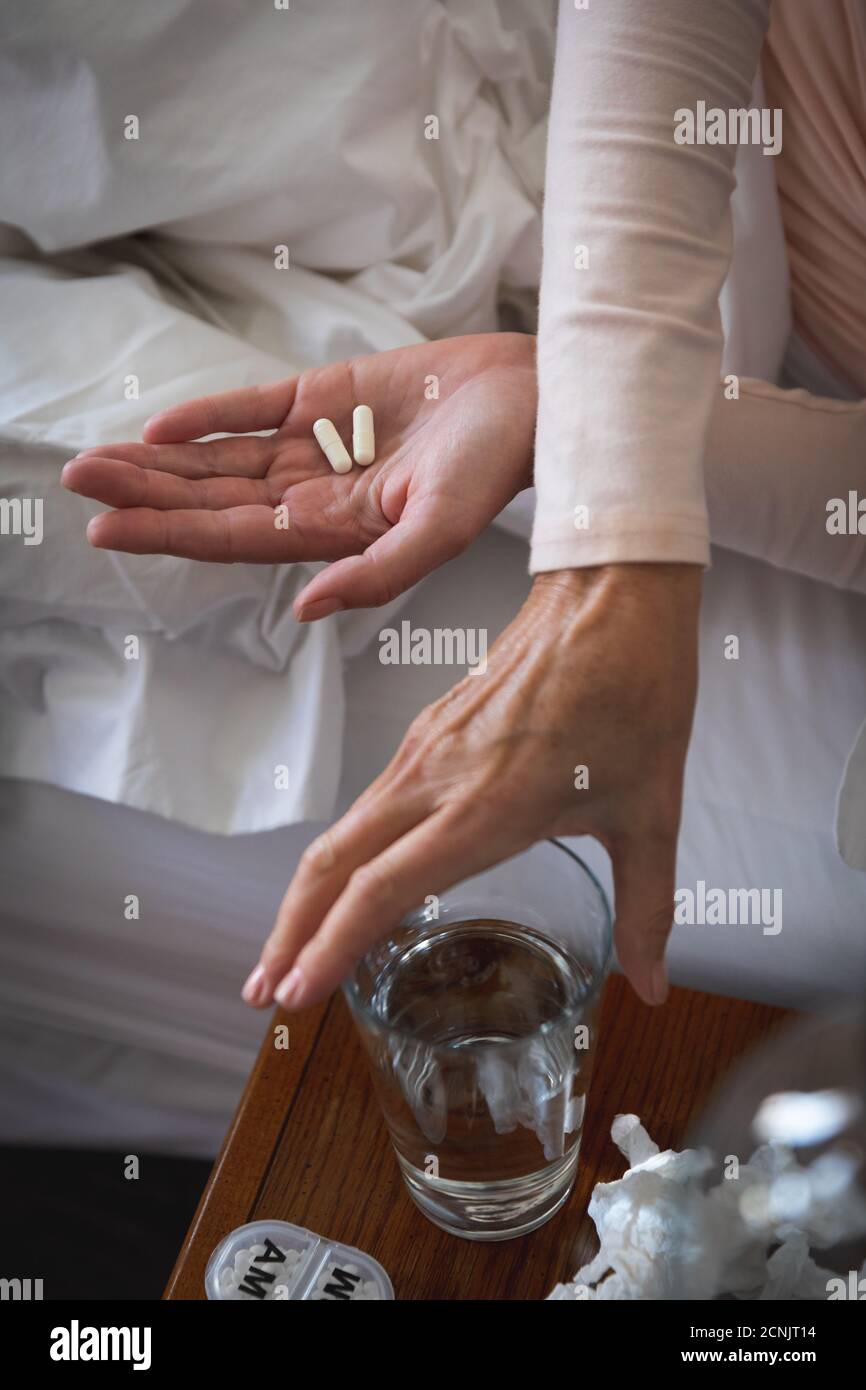 Mid section of sick Caucasian woman spending time at home, social distancing and self isolation in quarantine lockdown, lying in bed, holding pills, r Stock Photo